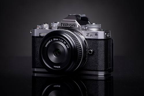 Серебристая Nikon Z fc с плоским объективом 28 мм на тёмном фоне