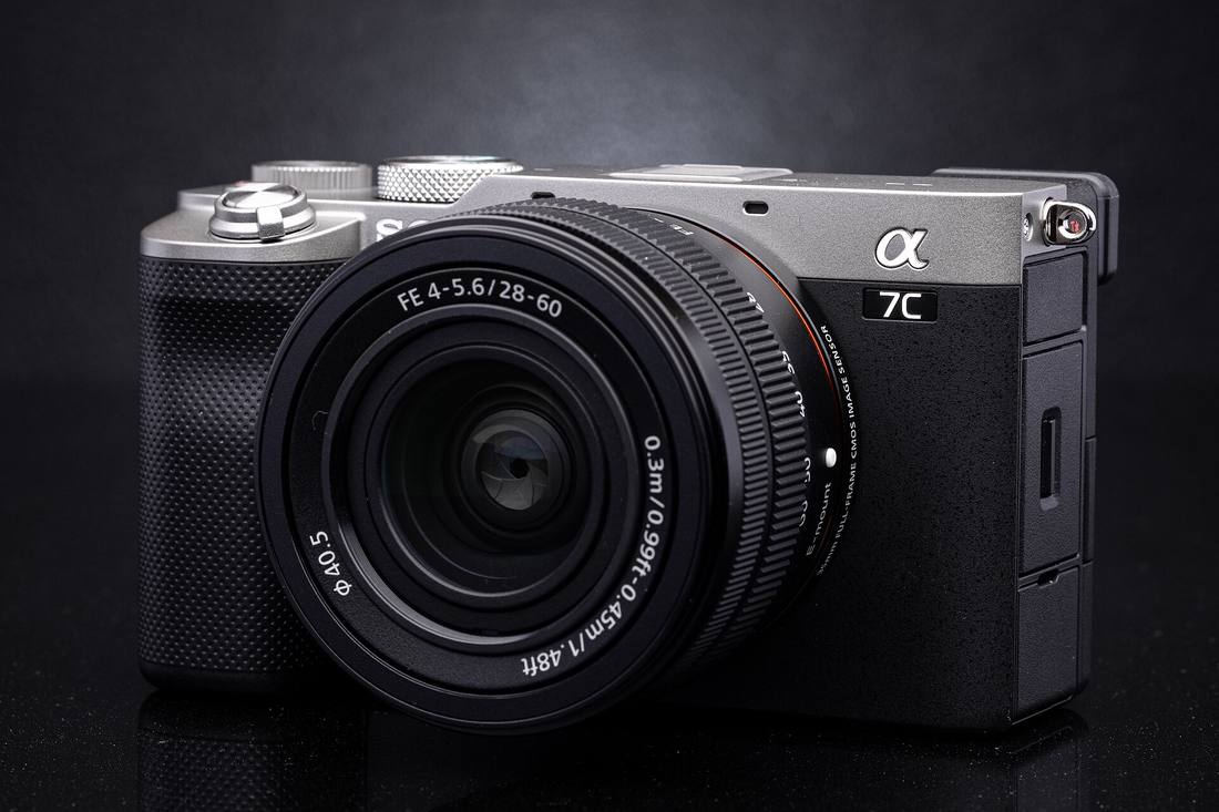 Серебристая Sony A7C с компактным зумом 28–60 мм на тёмном фоне